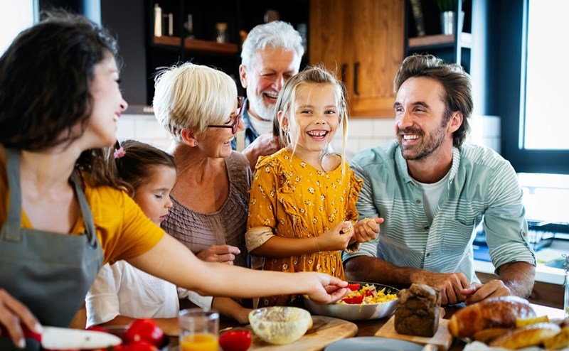 A large group of people smiling and cooking in the kitchen.
