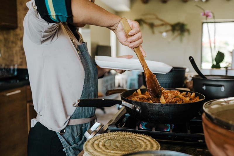 Woman wearing an apron holding a wooden spatula in the kitchen.