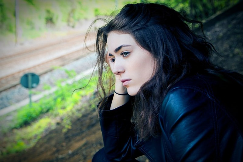 Thoughtful young woman sitting by train tracks, looking pensive and distant