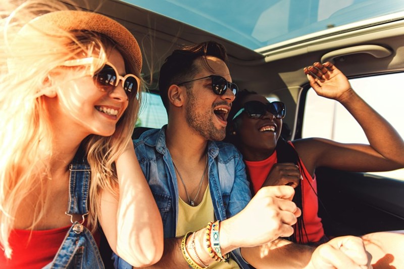 Group of friends laughing and enjoying a sunny road trip together in a car
