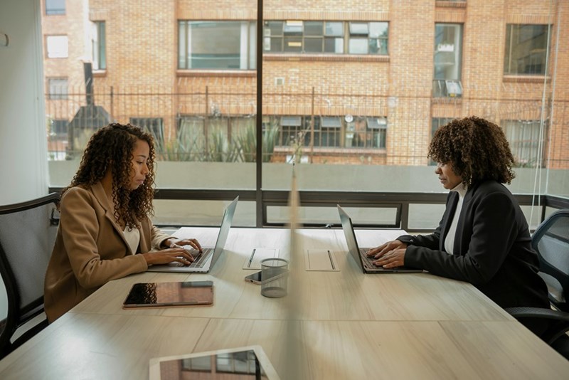Two women sitting at work table with laptops