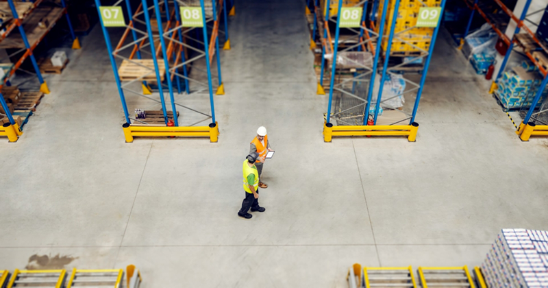 Top-down view of two warehouse employees in safety gear walking between the aisles in a warehouse