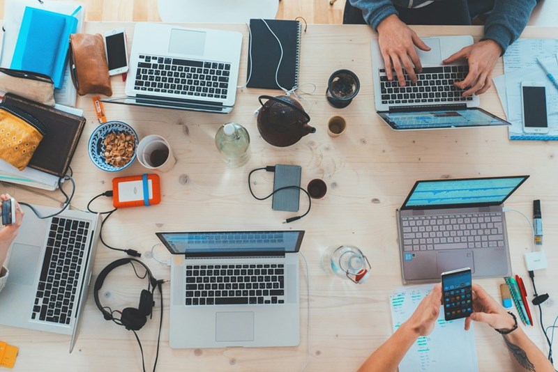 An overhead shot of startup employees working at a communal desk on their laptops.