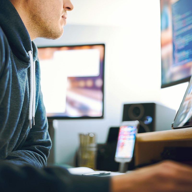 A tech employee works at his desk with multiple monitors and a phone setup in front of him.