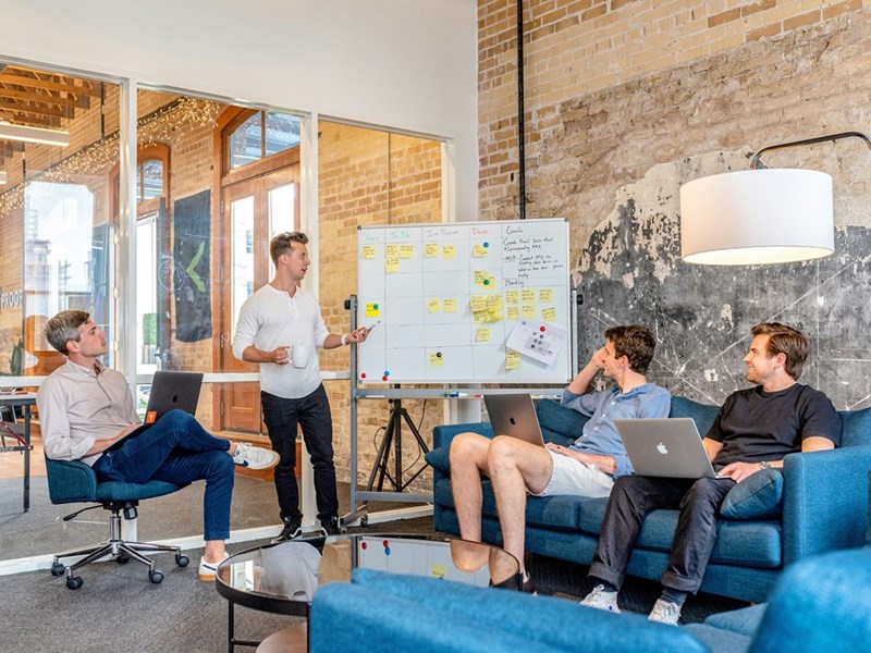 A group of startup employees meets as their manager addresses them in front of a whiteboard.