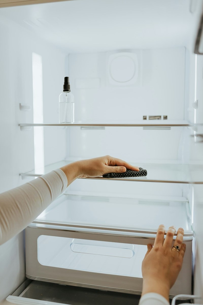 Person cleaning and organizing empty refrigerator shelves with cloth, maintaining hygiene in kitchen