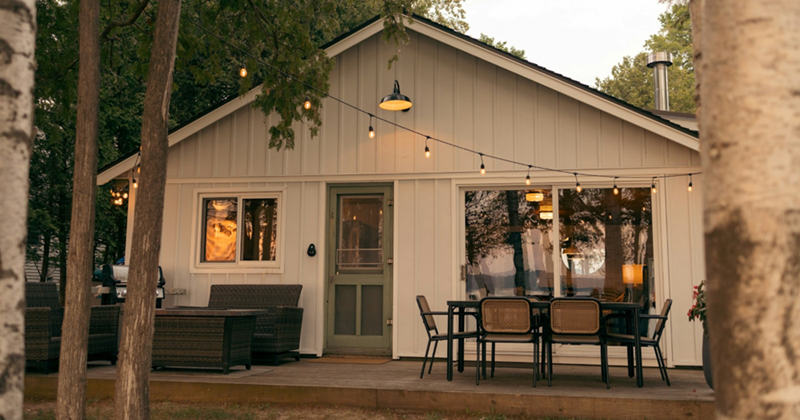 A small, single-storey house with outdoor lights and seating in front of it