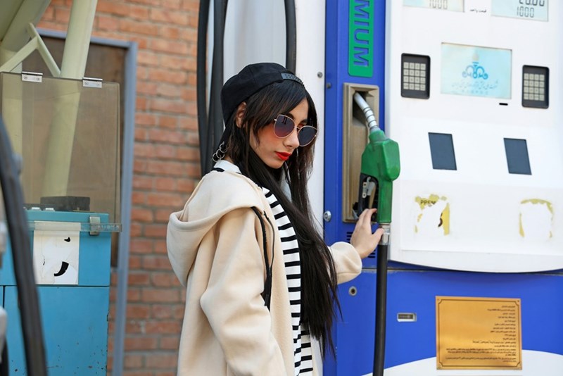 Woman stands by gas pump.
