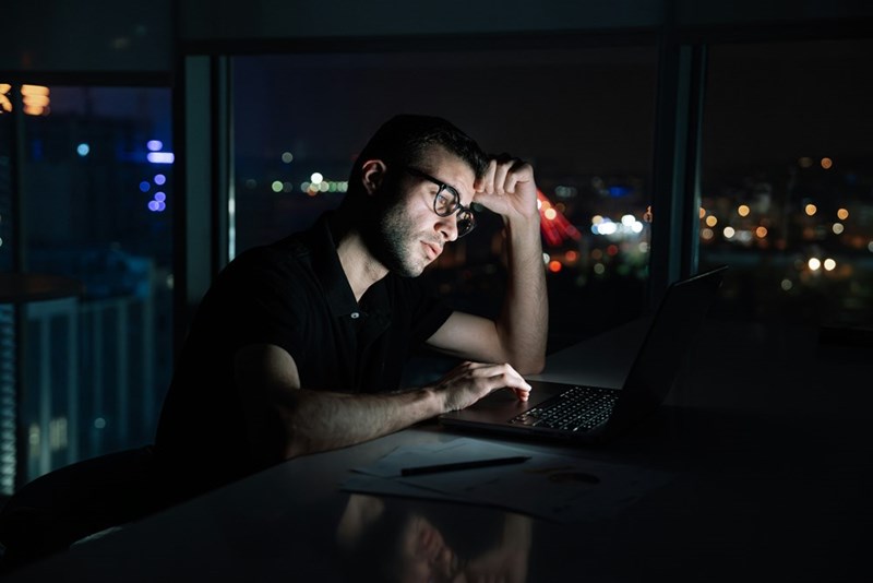 A man sits in front of a laptop late at night