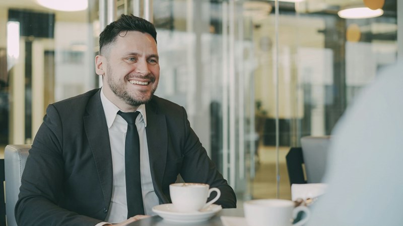 A man sits smiling at a table with coffee