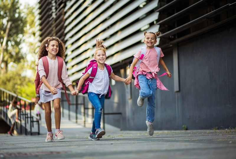 Happy group of girls leaving school for the day while wearing their backpacks.