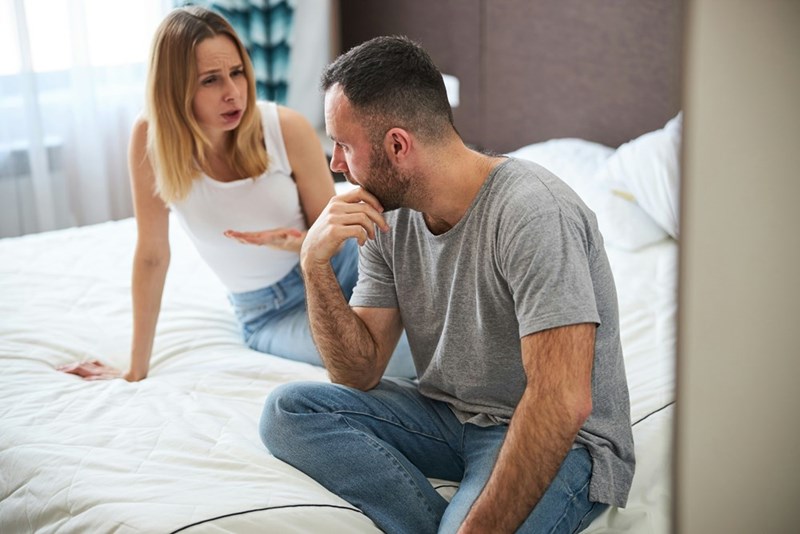 Couple sitting in the bed wearing casual clothes having a discussion.