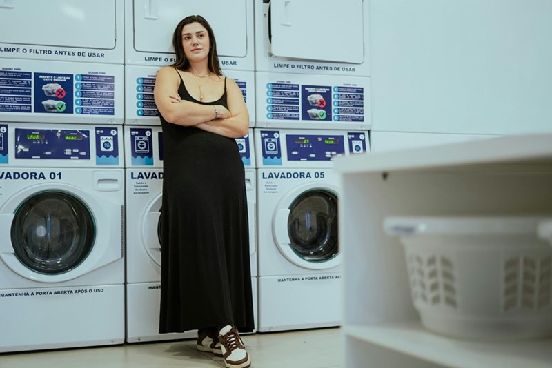 Woman wearing a black romper crossing arms in a laundry room.