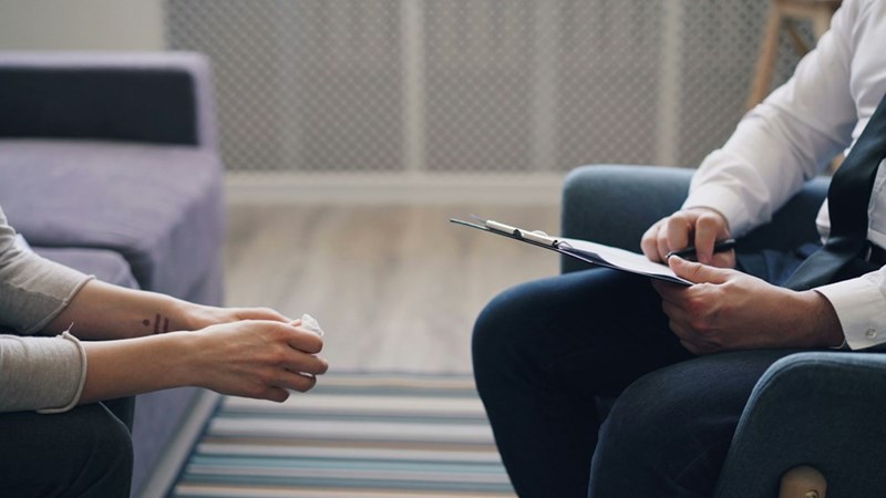 A counselor listens attentively to a student, holding notes in a quiet, private office setting.