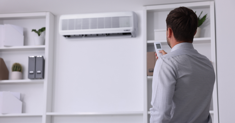 Man Switching on Air Conditioner with Remote Control in Office