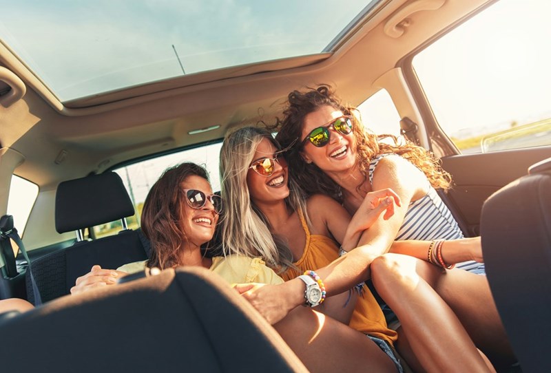 Women smile and laugh while sitting in the back seat of a car together.