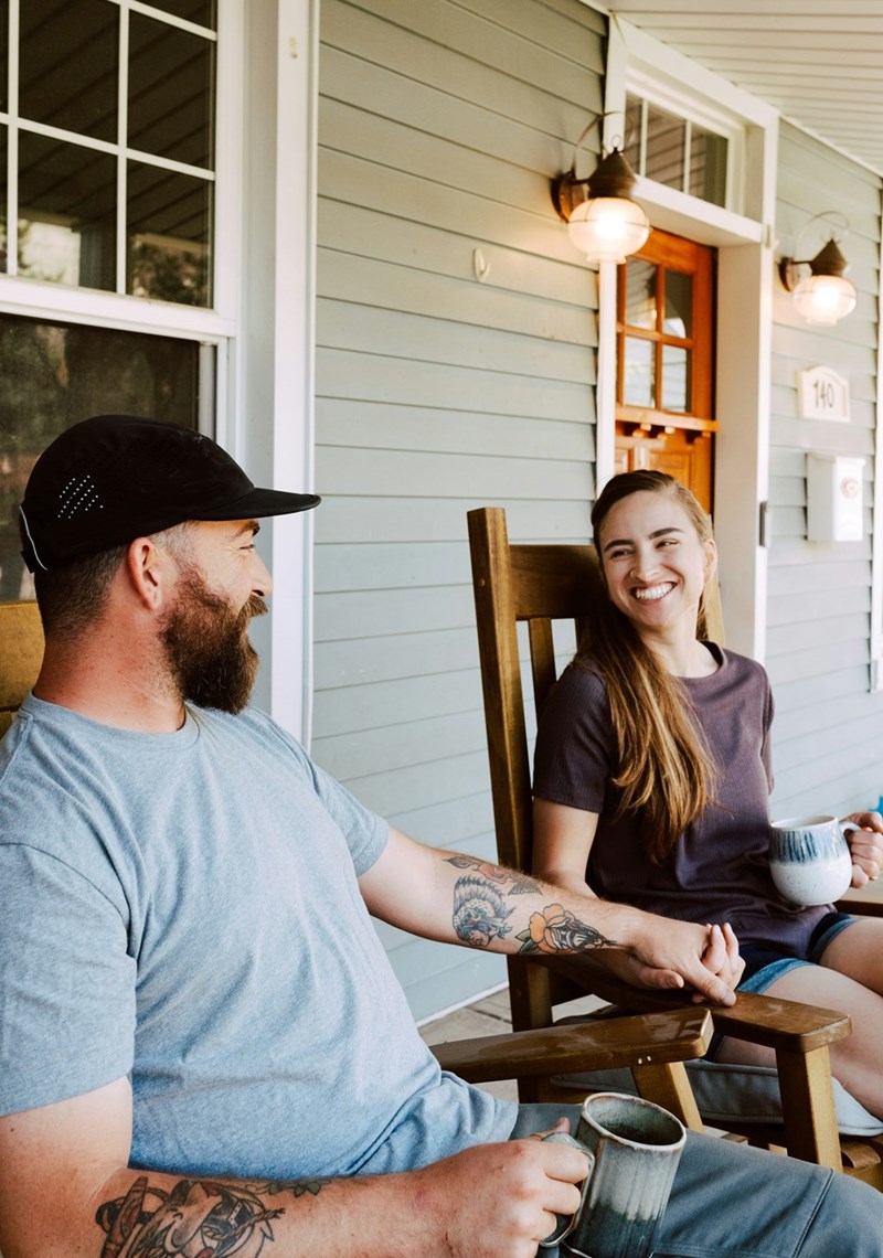 Happy couple sitting on their front porch drinking coffee, smiling, and holding hands