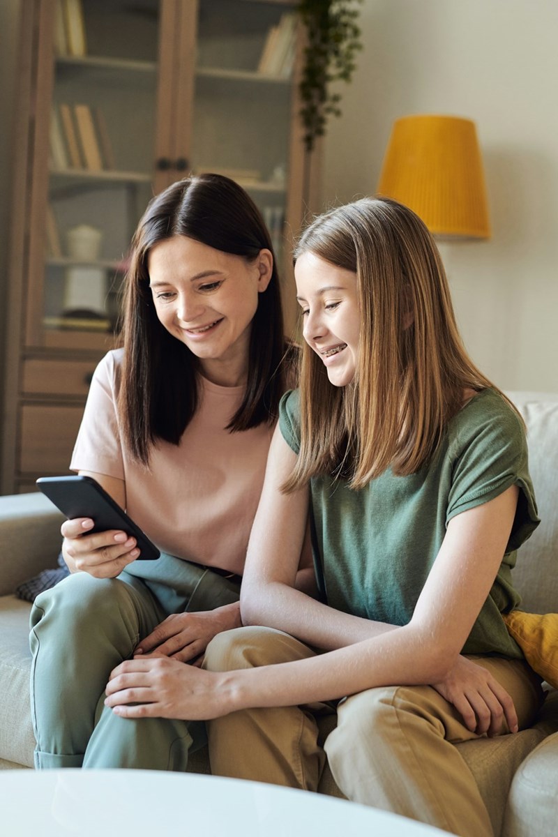 Mother and pre-teen daughter laugh together at something on the cellphone