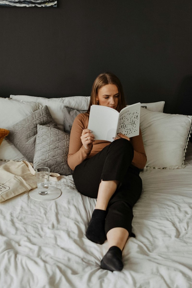 A woman sitting on a bed reading a book