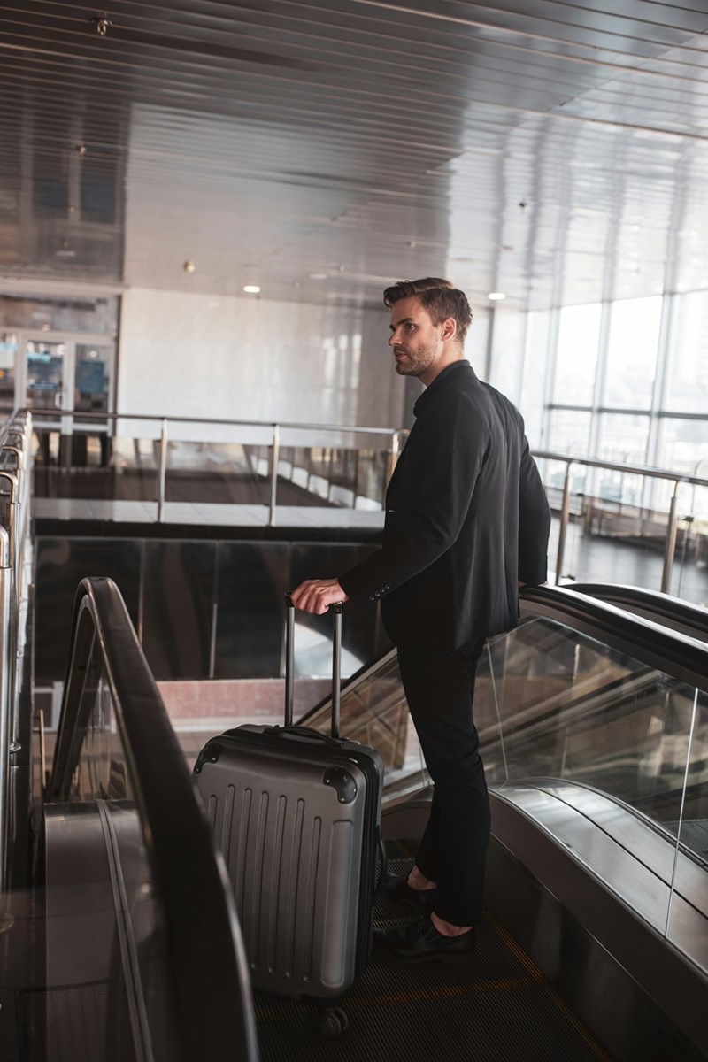 Man in a suit traveling in the airport with a rolling carry-on bag headed to his flight gate