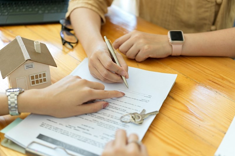 A tenant signs a rental agreement while reviewing documents and keys sit nearby on the table.