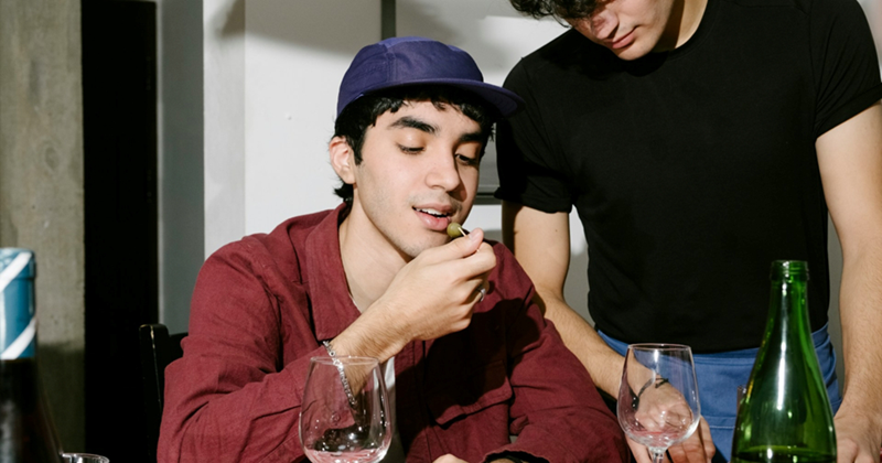 A young man sitting in a restaurant eats an olive off a toothpick with a server standing over him