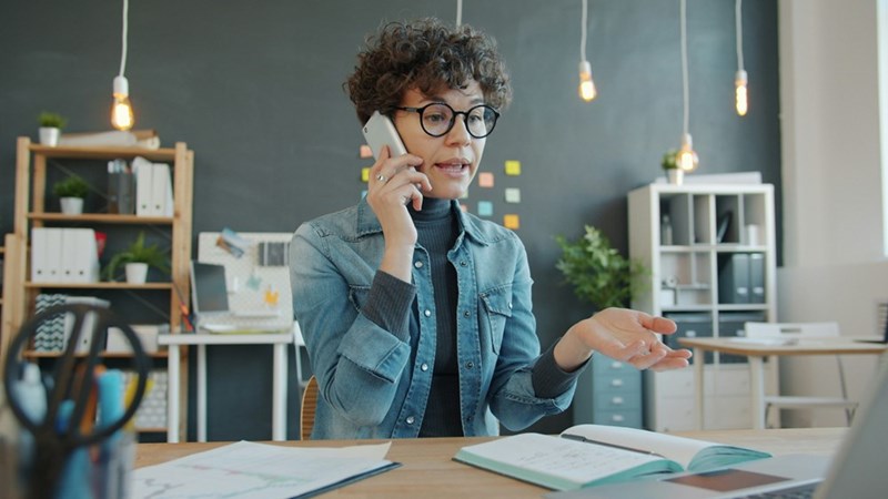 An upset woman talks on the phone at her desk