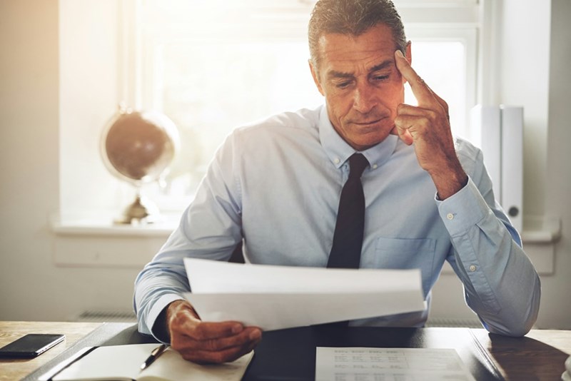 Mature businessman wearing a shirt and tie reading documents while sitting alone at his desk in an office