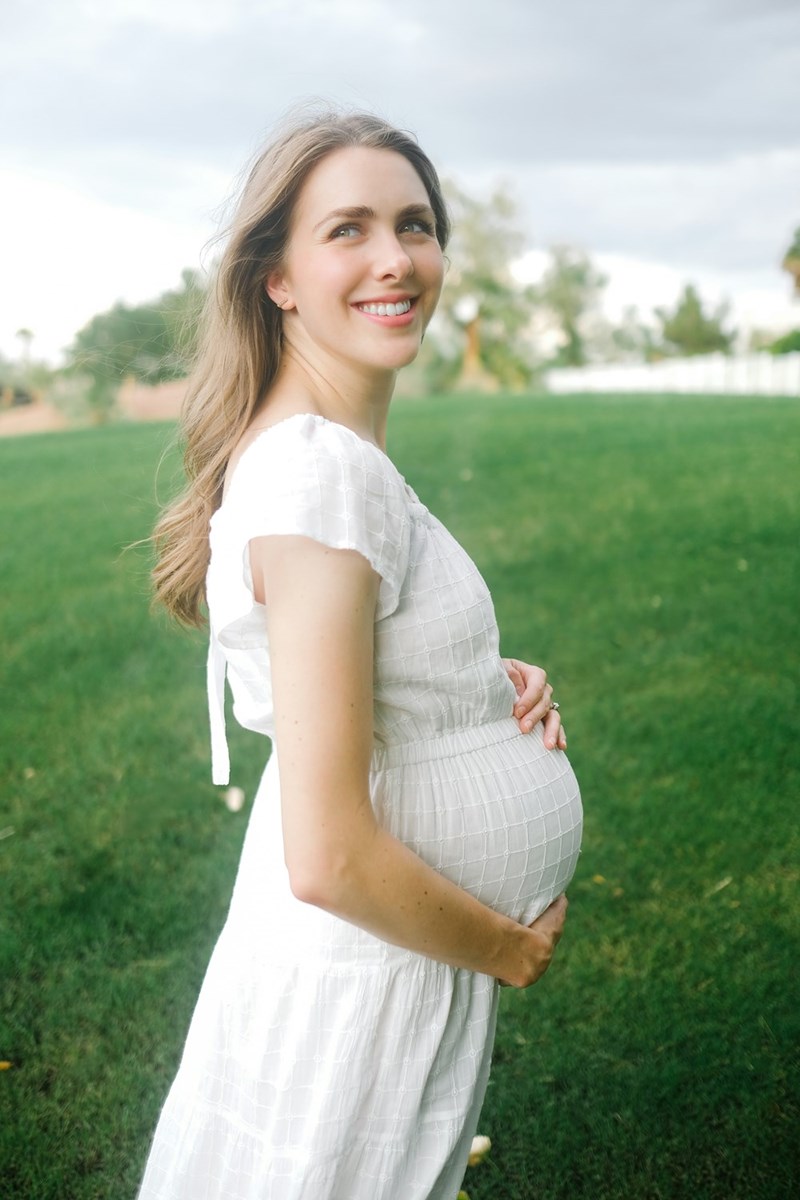 A pregnant woman in a white dress poses for a picture