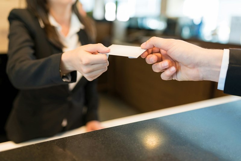 A female front desk agent hands a room key to a hotel guest.