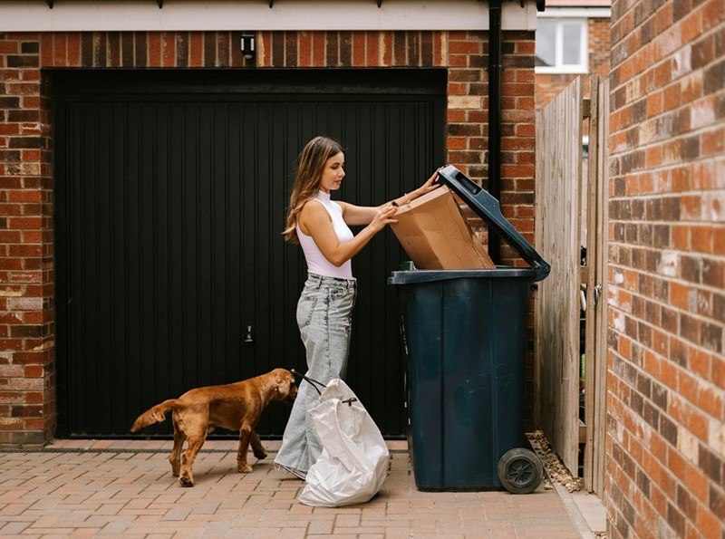 A woman takes out the trash as her dog follows her.