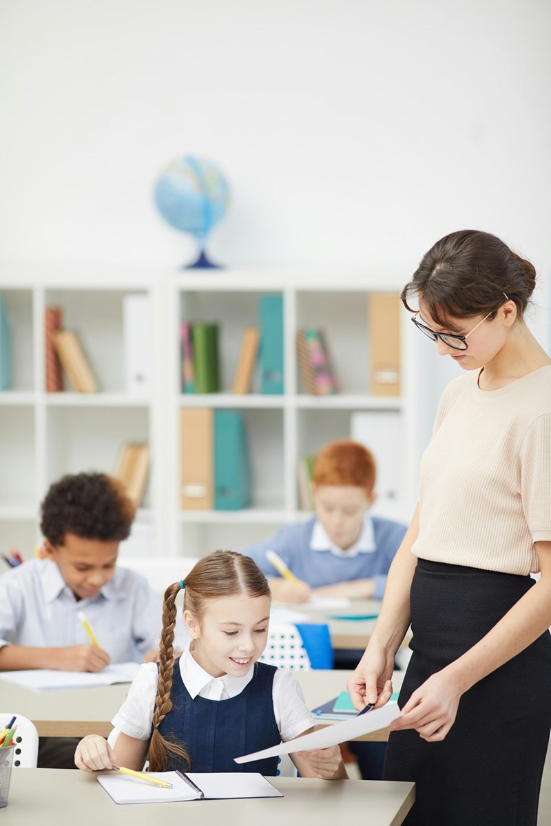 A portrait of a female teacher assisting a student in class.