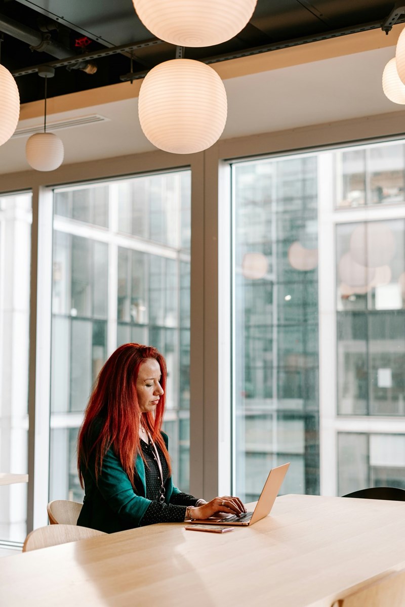 A red-headed employee sits at her work station wearing headphones in the office.