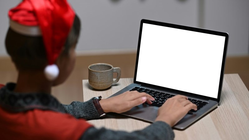 A designer woman in Christmas hat is working on laptop with blank screen in office