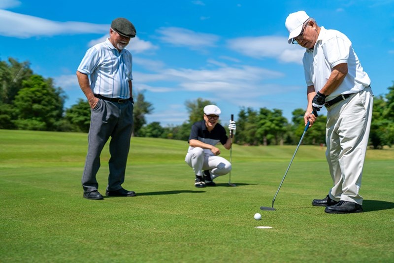 2 golfers watch closely while one member of their group putts close to the hole.