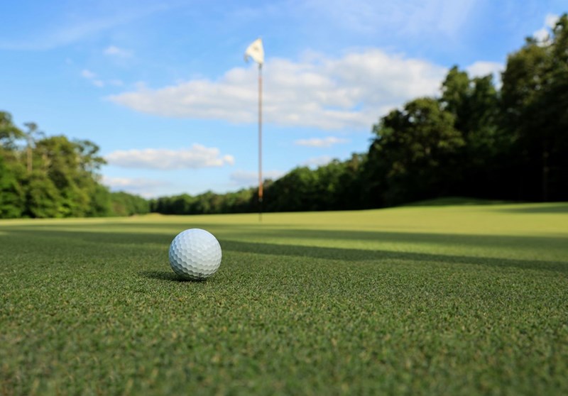 Golf ball sitting in front of flag on golf course on a beautiful sunny day.