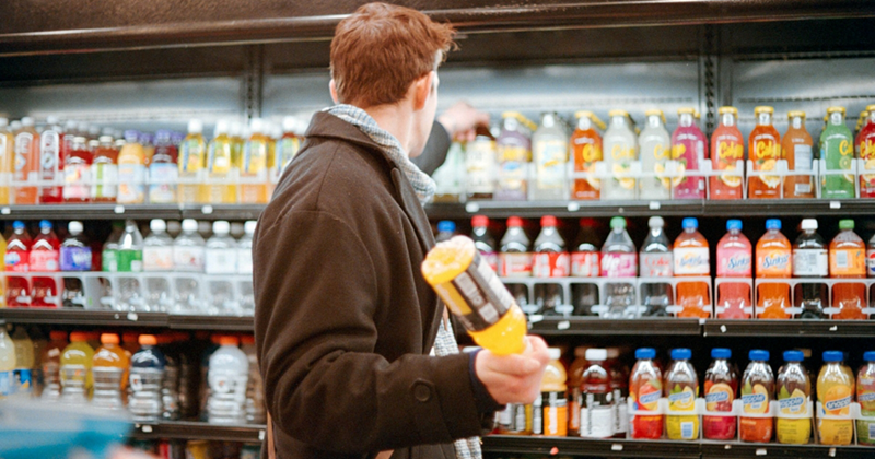 A male customer browsing the chilled drinks aisle with a bottle in his hand