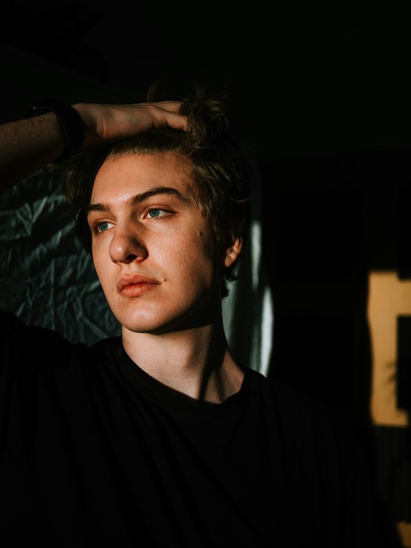 Young man in dramatic lighting looks off into the distance with a serious, contemplative expression.