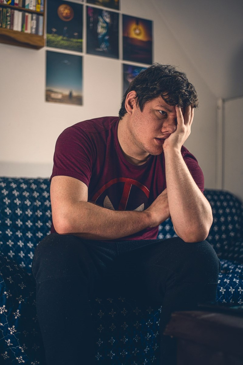 Young man sitting on a couch with his head in his hand, looking emotionally drained or frustrated.