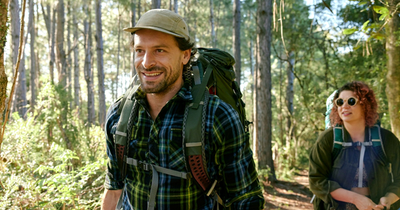 Front view of a man hiking through a forest with a woman behind him