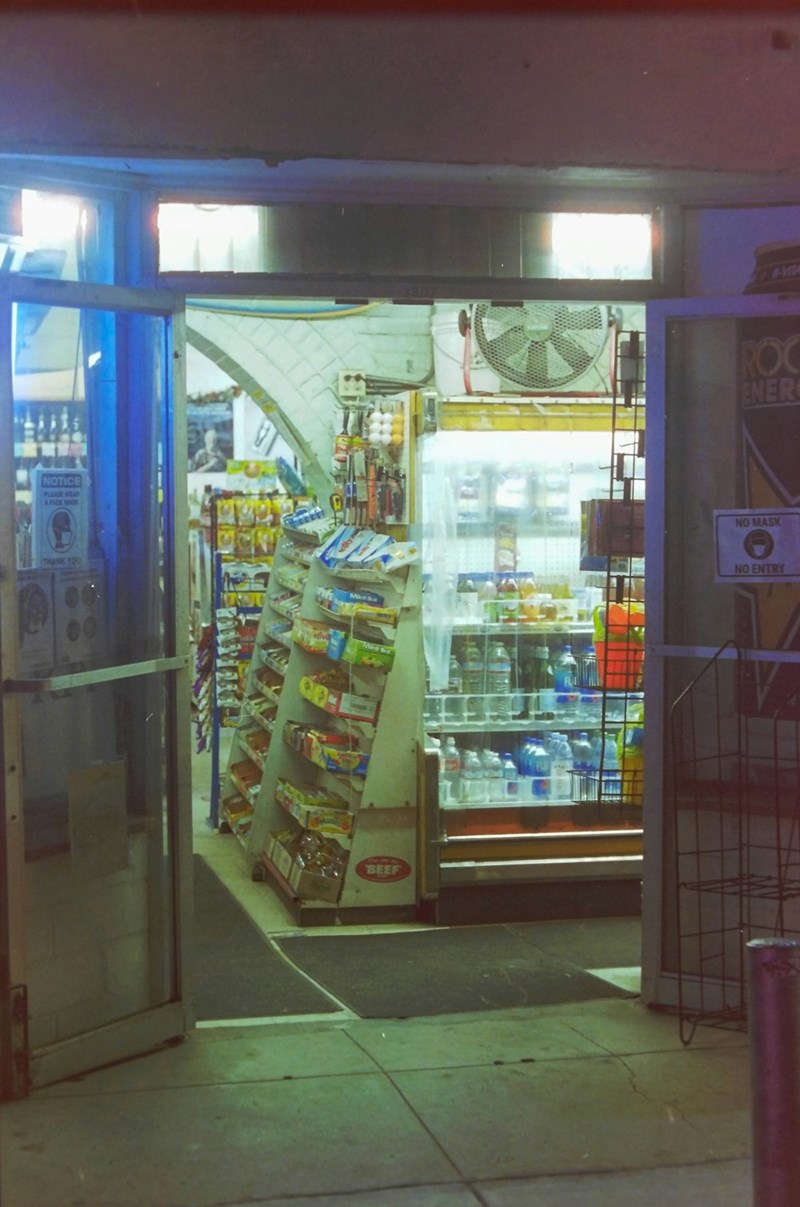 Inside of a convenience store, dimly lit and fully stocked with snacks and other boxed goods