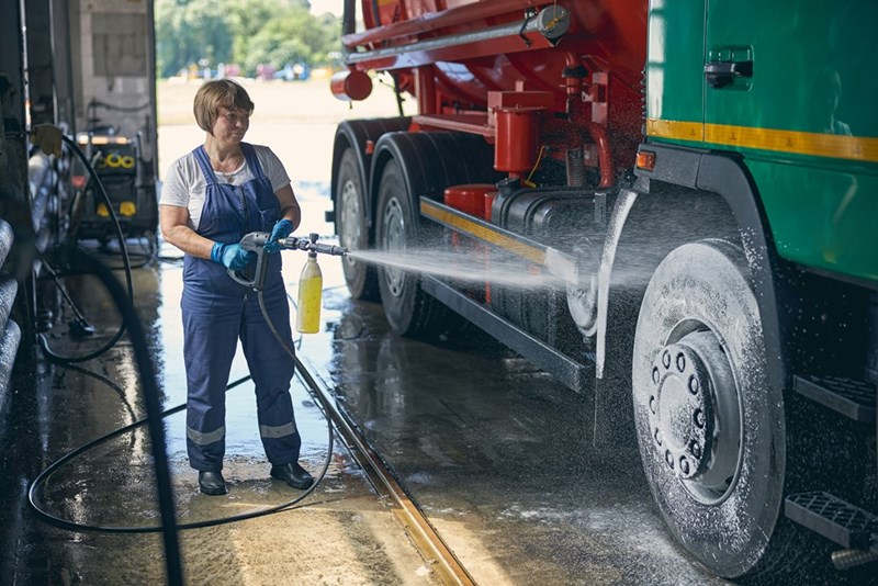 Worker pressure washes a large truck.