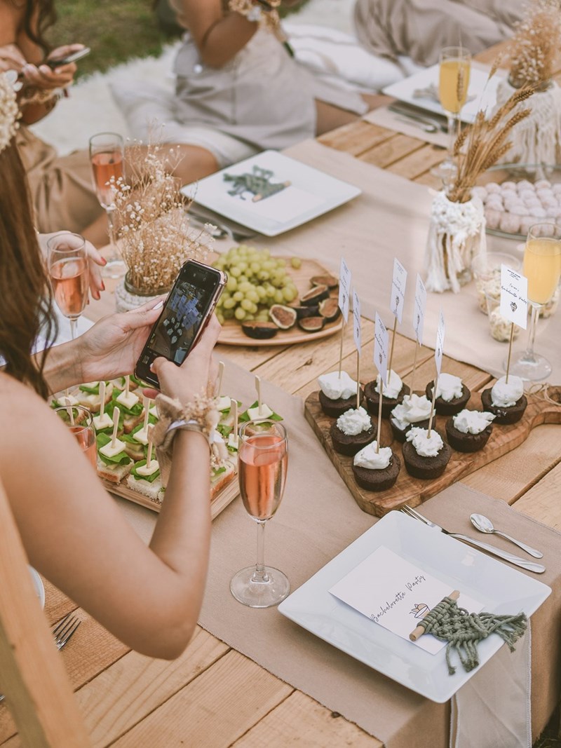 Woman taking photos of an elegant meal set up on a picnic table for a bachelorette party
