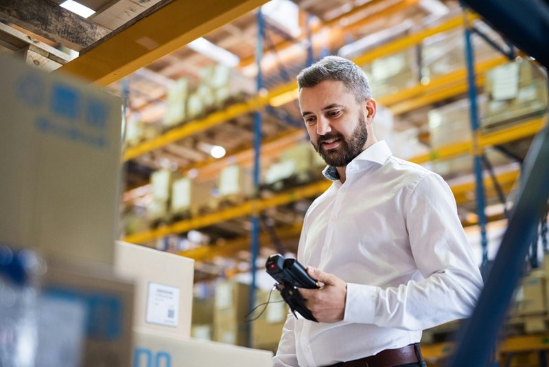 A warehouse supervisor wears a button-down shirt while holding a barcode scanner.