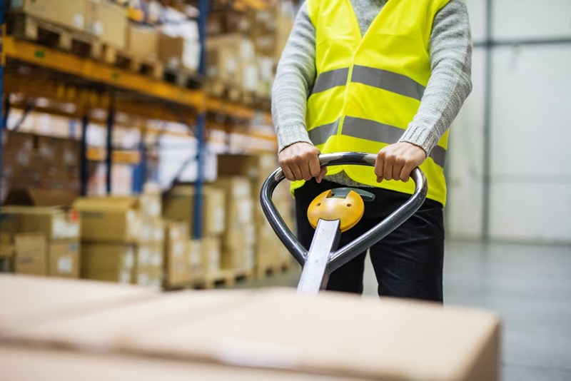 A warehouse employee pulls a pallet truck with boxes.