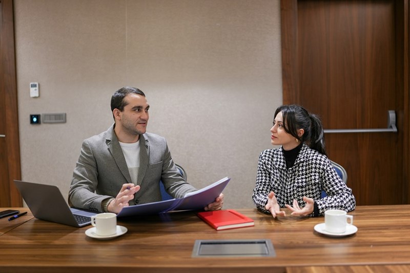 A man sits at a table wearing a jacket in front of a laptop next to a recruiter.