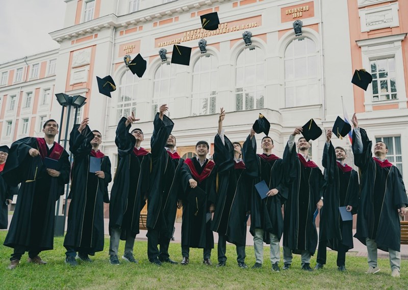 A group of graduates celebrates by tossing their caps into the air outside a university building.