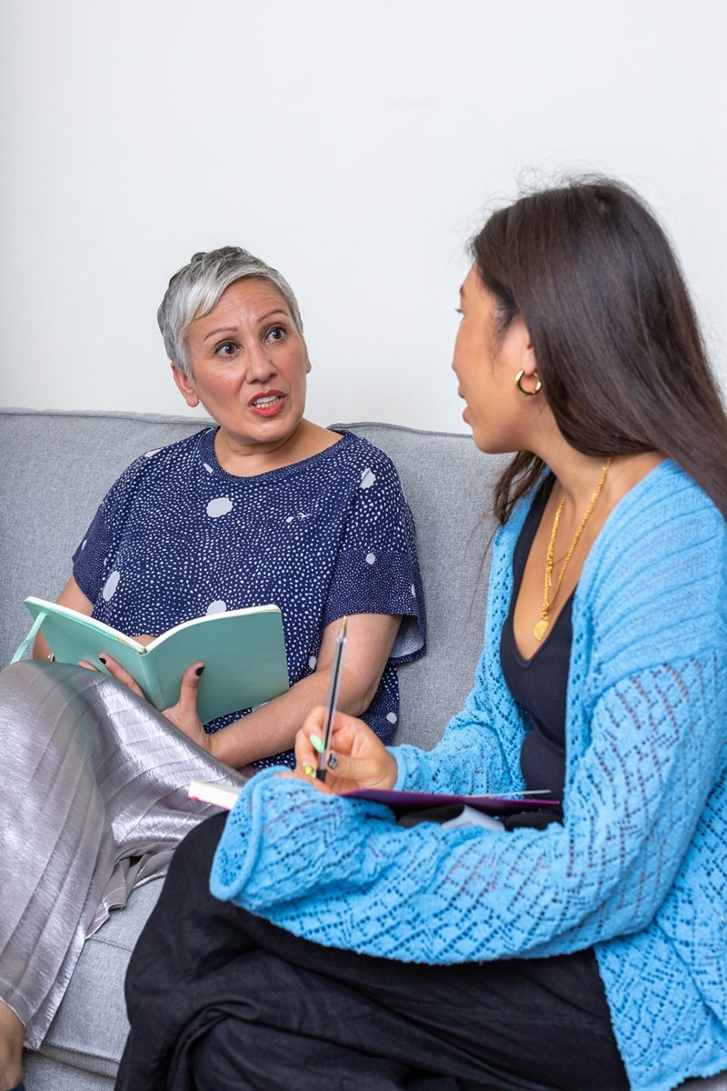 Two women discussing notes together during focused conversation on living room couch.