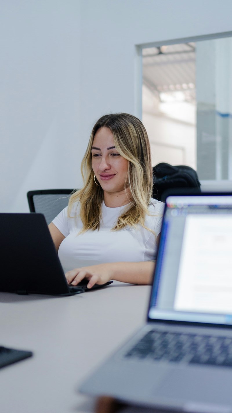 Woman smiling while working on laptop in modern office workspace.