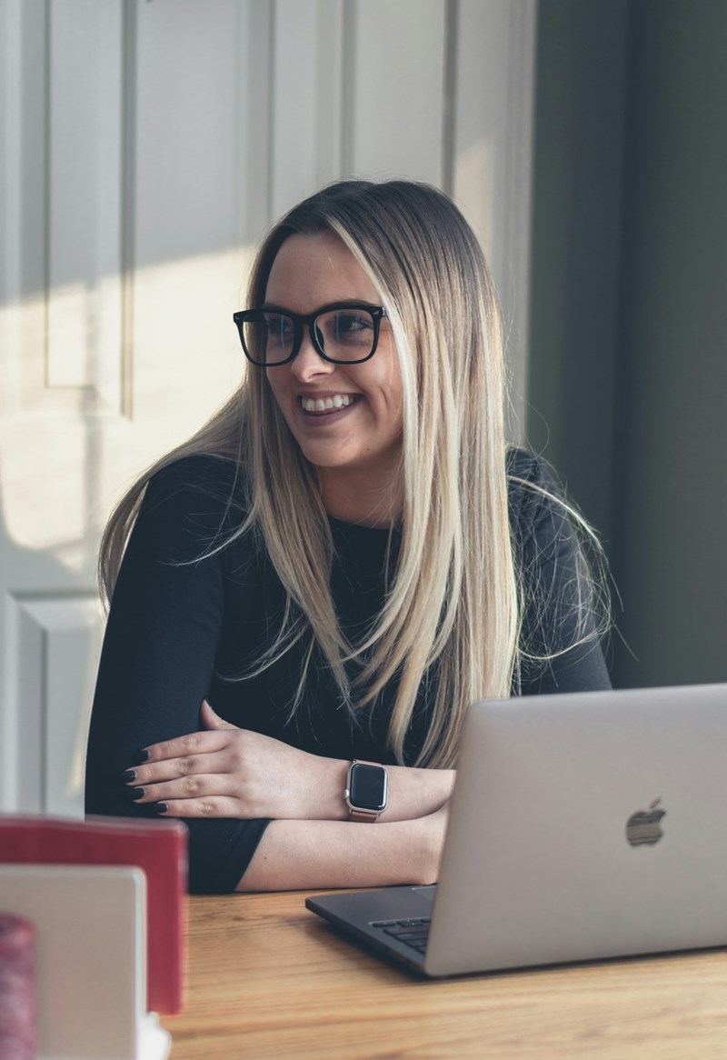 Smiling woman with glasses using laptop at office desk during work meeting.